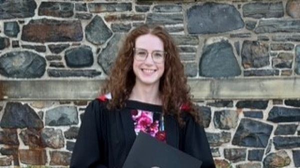 Annie standing in front of a stone wall in a graduate gown