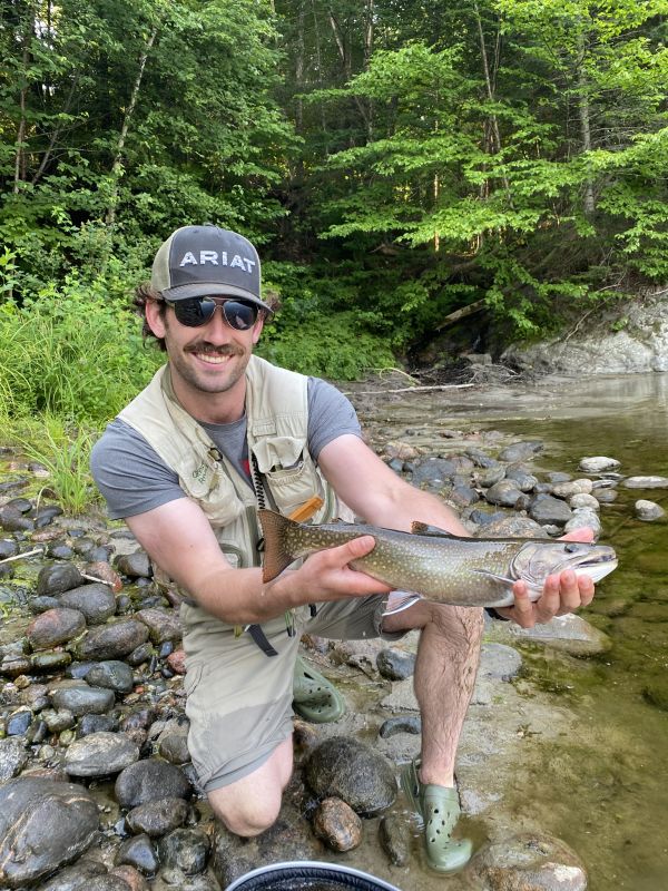Gavyn holding a fish at a river edge