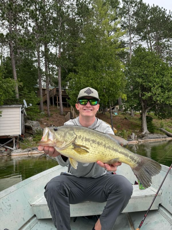 Josh in a boat with trees behind him. Josh is holding a big Bass