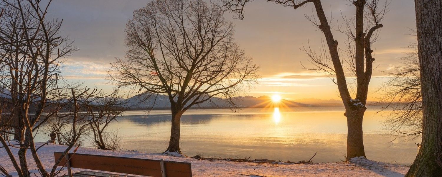 Wooden Bench in the snow overlooking the lake and sunrise