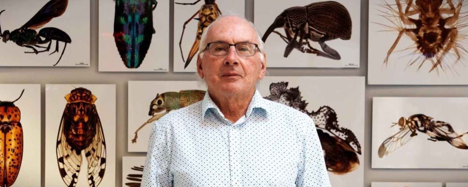 Photo of Paul herbert in front of a wall of photos of insects