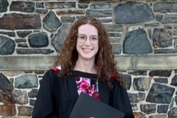 Annie standing in front of a stone wall in a graduate gown