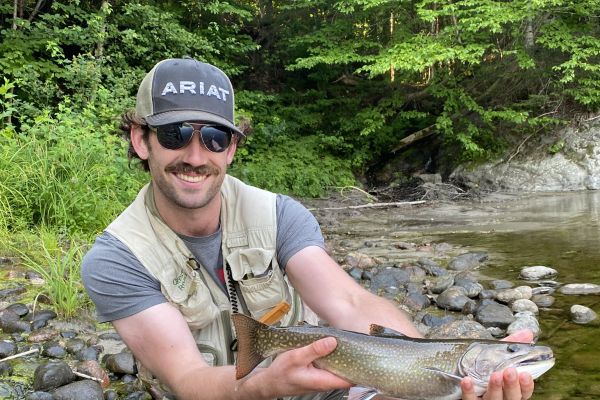 Gavyn holding a fish at a river edge